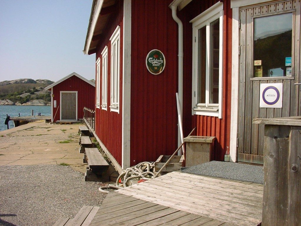 Den röda boden med trädäck och sjöboden i bakgrunden