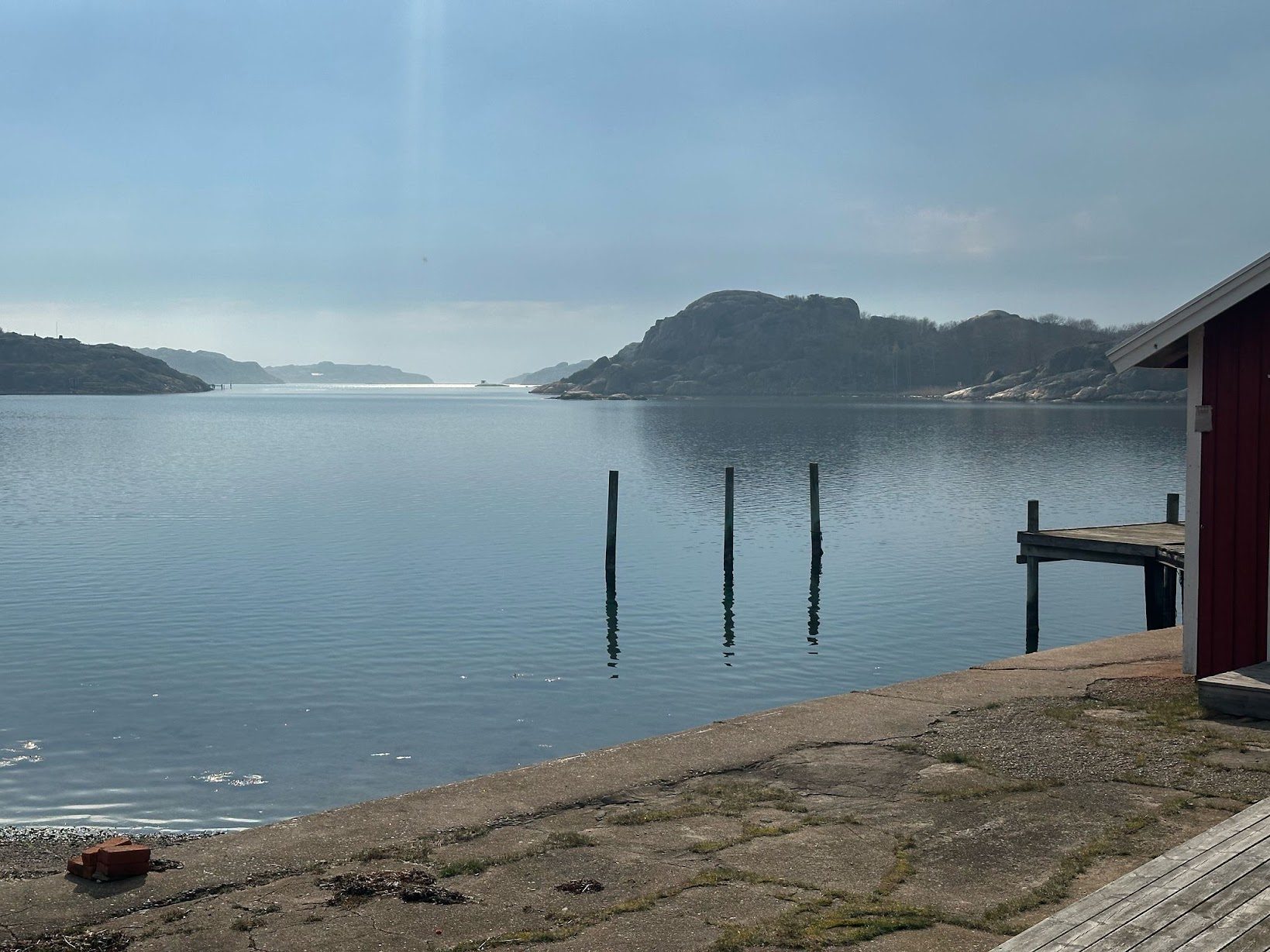 Förtöjningspålar och brygga vid den röda boden en stilla morgon