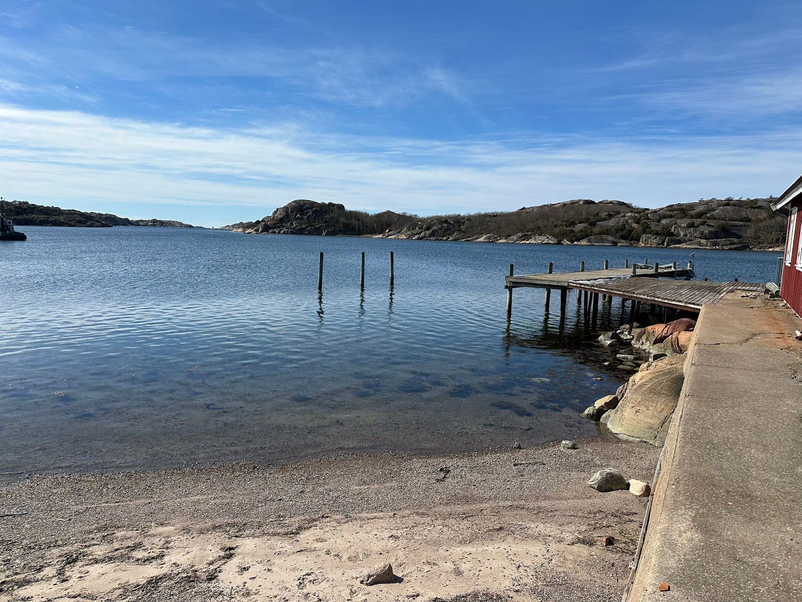 Den privata sandstranden vid bryggan, med pålar i vattnet och kala klippor på andra sidan sundet